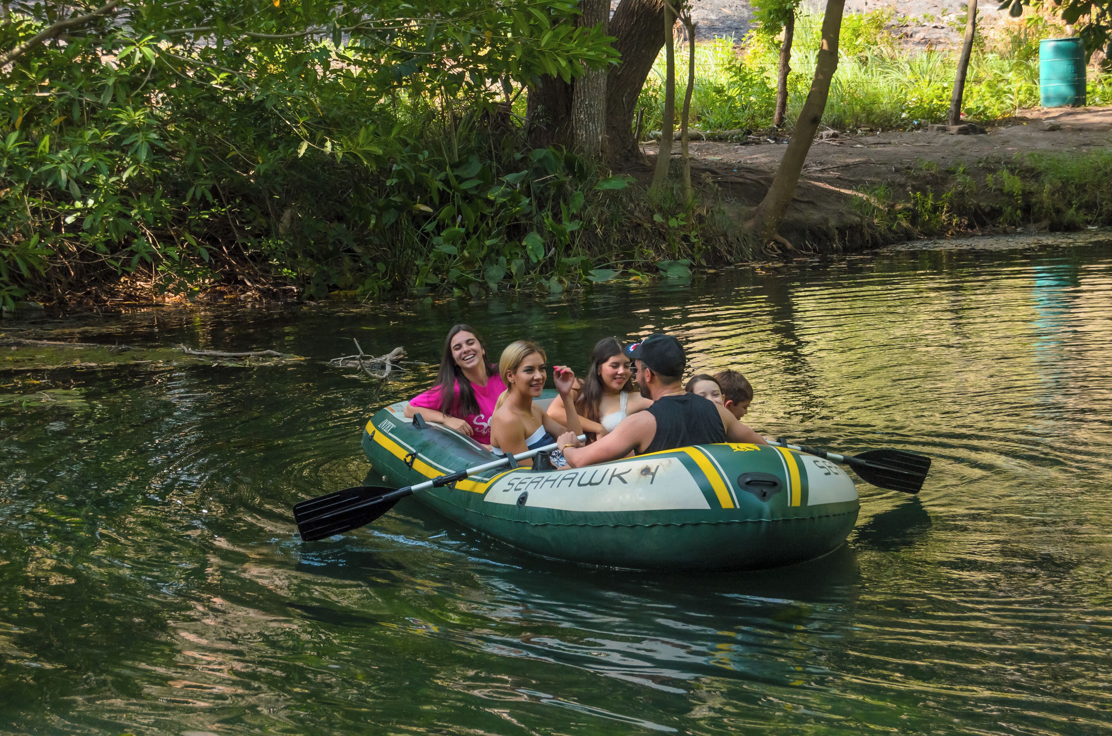 A group of people in a green inflatable raft on a calm river surrounded by greenery.