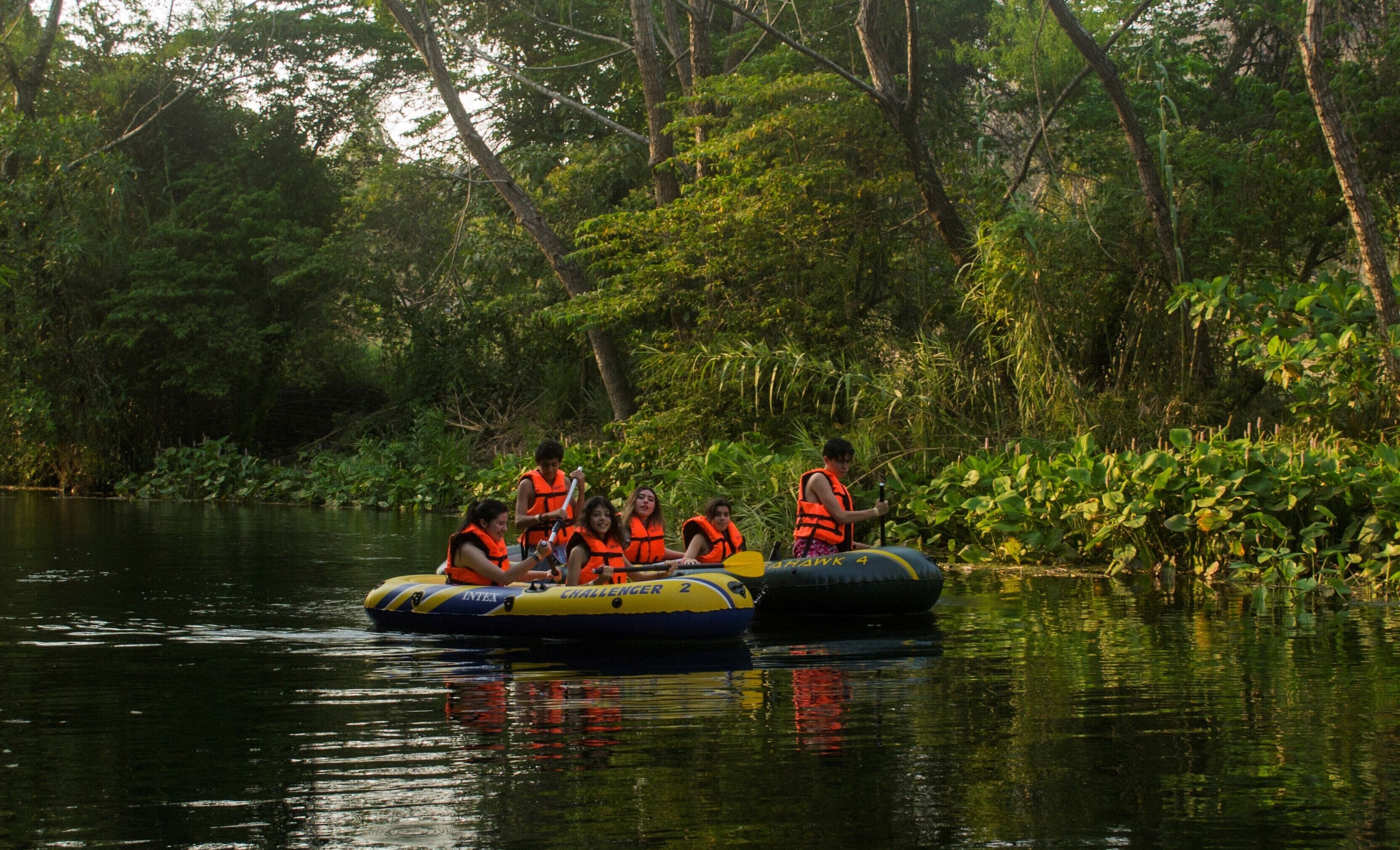 Un groupe de personnes à bord de radeaux gonflables sur une rivière paisible, entourée d’une végétation luxuriante.