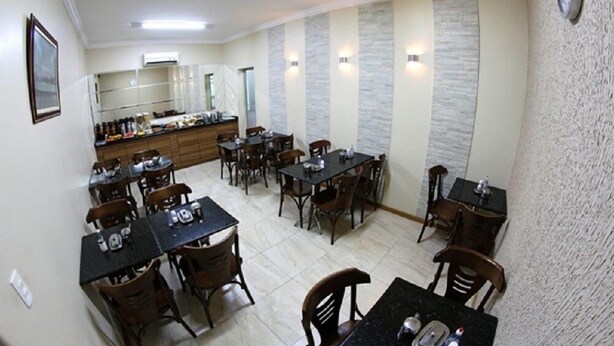 Un comedor con varias mesas y sillas, una zona de cocina con mostrador y electrodomésticos, y un reloj en la pared.