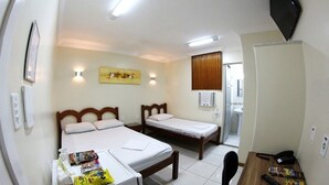 Habitación de hotel con dos camas individuales, un escritorio de madera con una silla, un refrigerador pequeño y un televisor montado en la pared.
