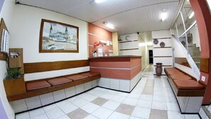 Un área de recepción con un banco, mostrador de recepción, un cuadro y una escalera.