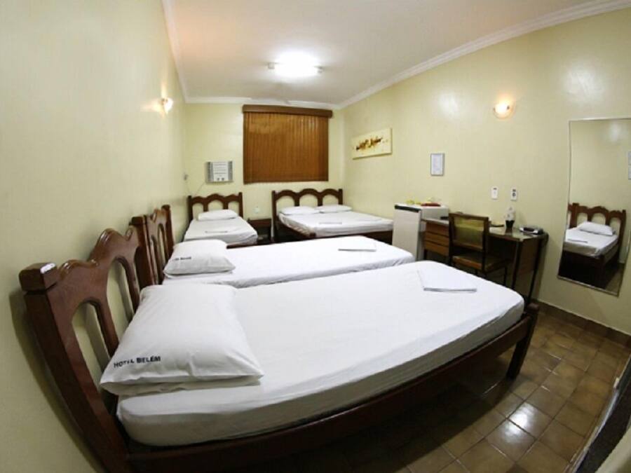 Ein Hotelzimmer mit zwei Einzelbetten, einem Holzkopfstück, einem Schreibtisch, einem Stuhl, einem Spiegel und einem Fenster mit Vorhängen.