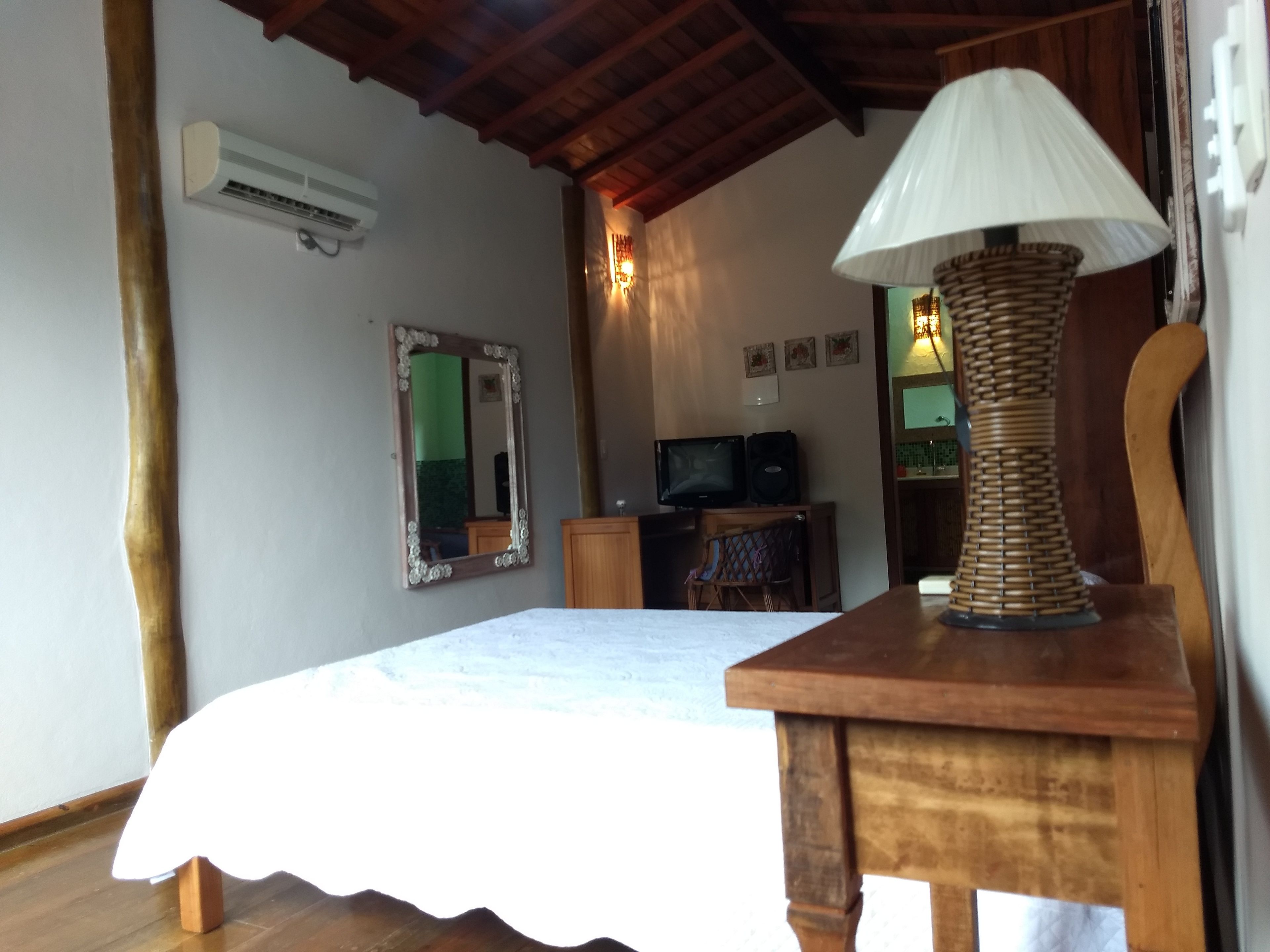 Un dormitorio con cama, mesita de noche de madera, lámpara, televisor y espejo.