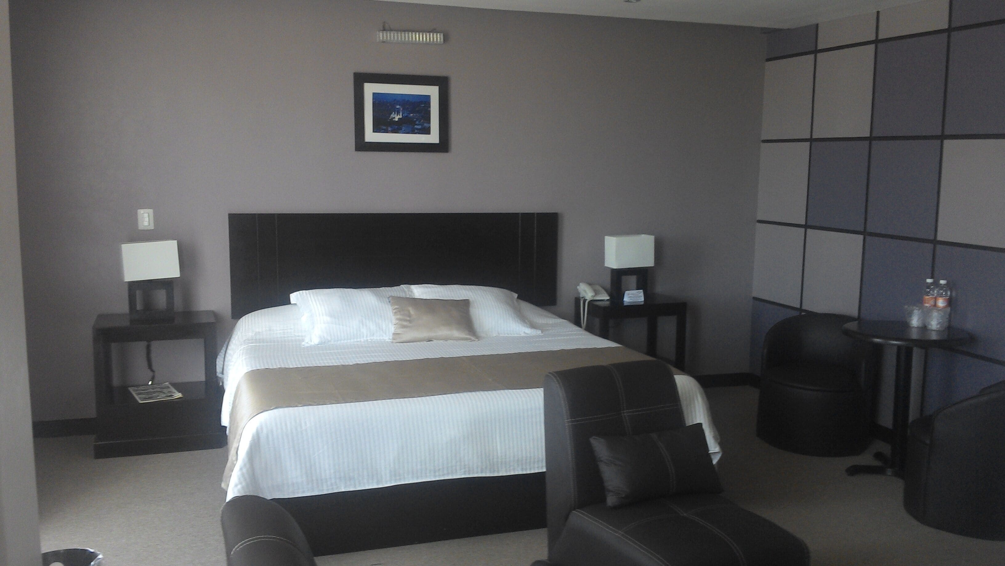 Una camera d'albergo con un letto grande, due comodini con lampade, una sedia e un quadro appeso al muro.