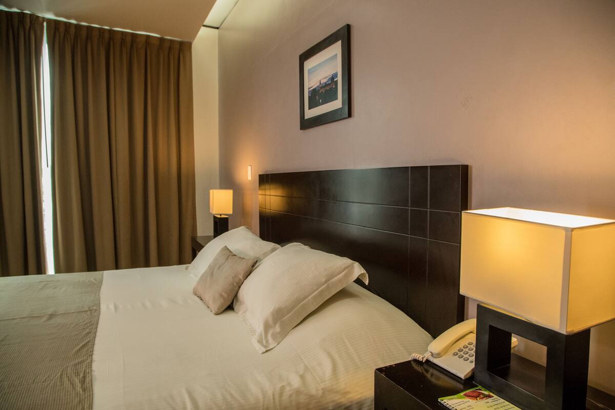 Habitación de hotel con una cama grande, dos lámparas de noche, un teléfono y un cuadro en la pared.