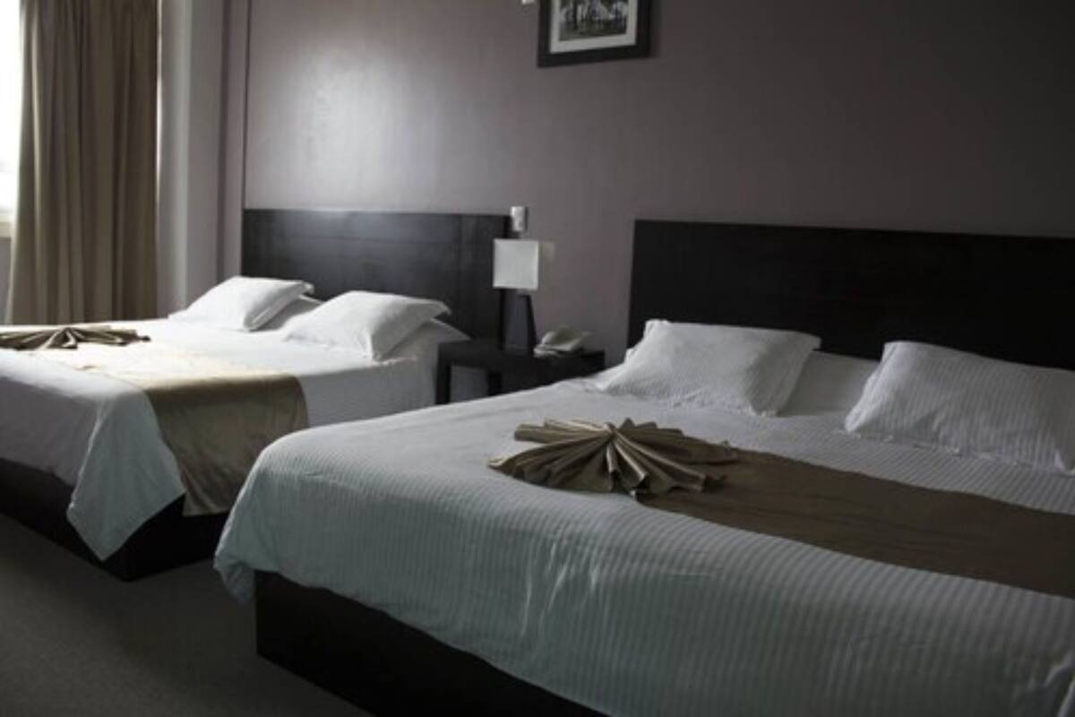 Una habitación de hotel con dos camas, una mesita de noche, una lámpara y un cuadro en la pared.