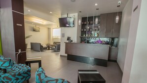 A modern hotel lobby with a bar area, seating, and a flat-screen TV. - Tierra Viva Hotel (Comitan de Dominguez)