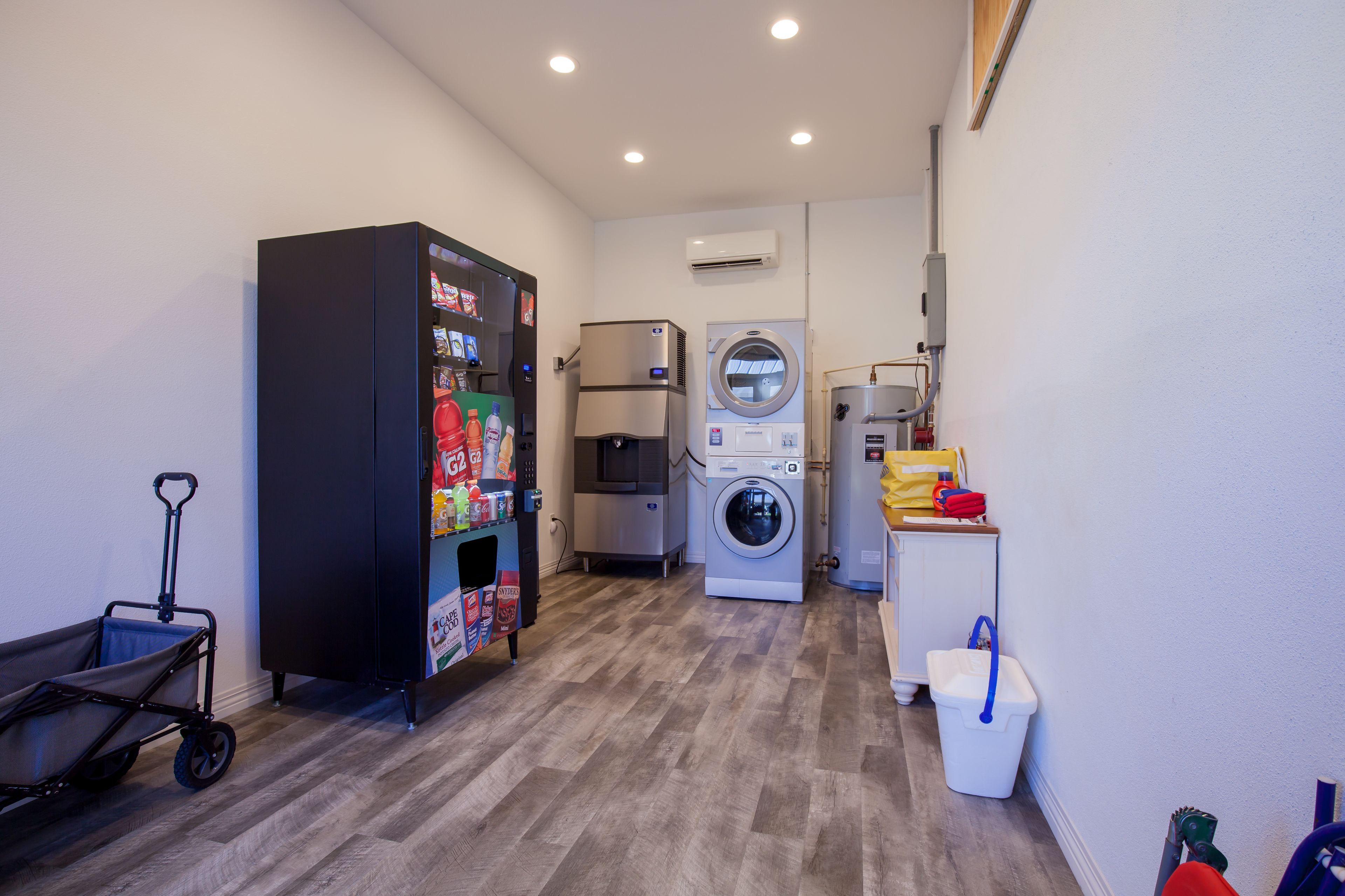 A laundry room with a vending machine, a washing machine, a dryer, and a cart.