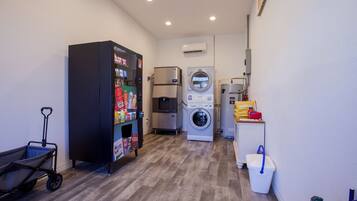 A laundry room with a vending machine, a washing machine, a dryer, and a cart.