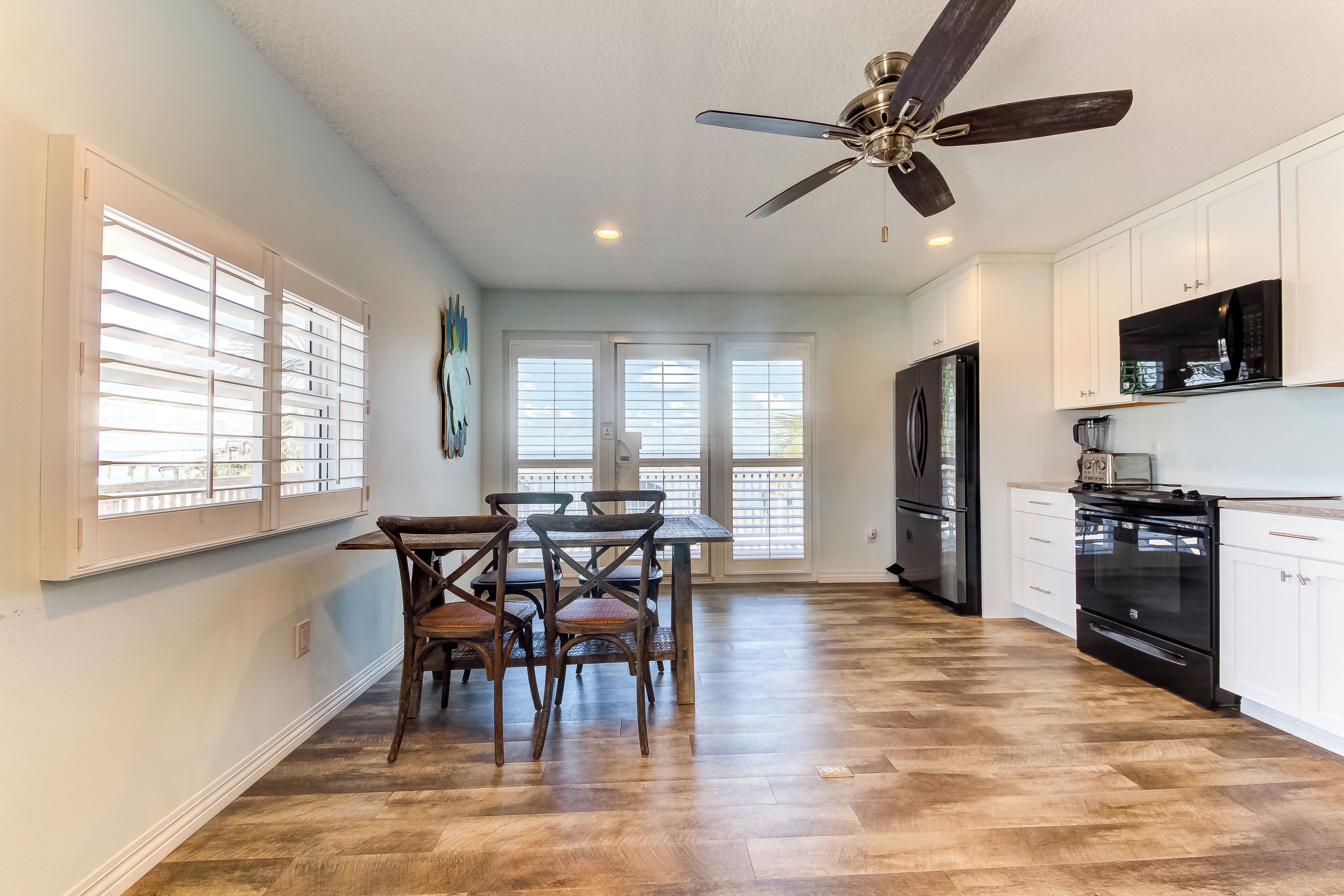 A kitchen with wooden flooring, white cabinets, a black refrigerator, and a ceiling fan.