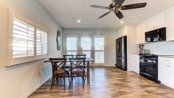 A kitchen with wooden flooring, white cabinets, a black refrigerator, and a ceiling fan.