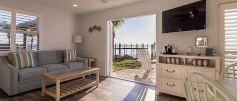 A living room with a sofa, coffee table, TV, and a view of the ocean through a sliding door.