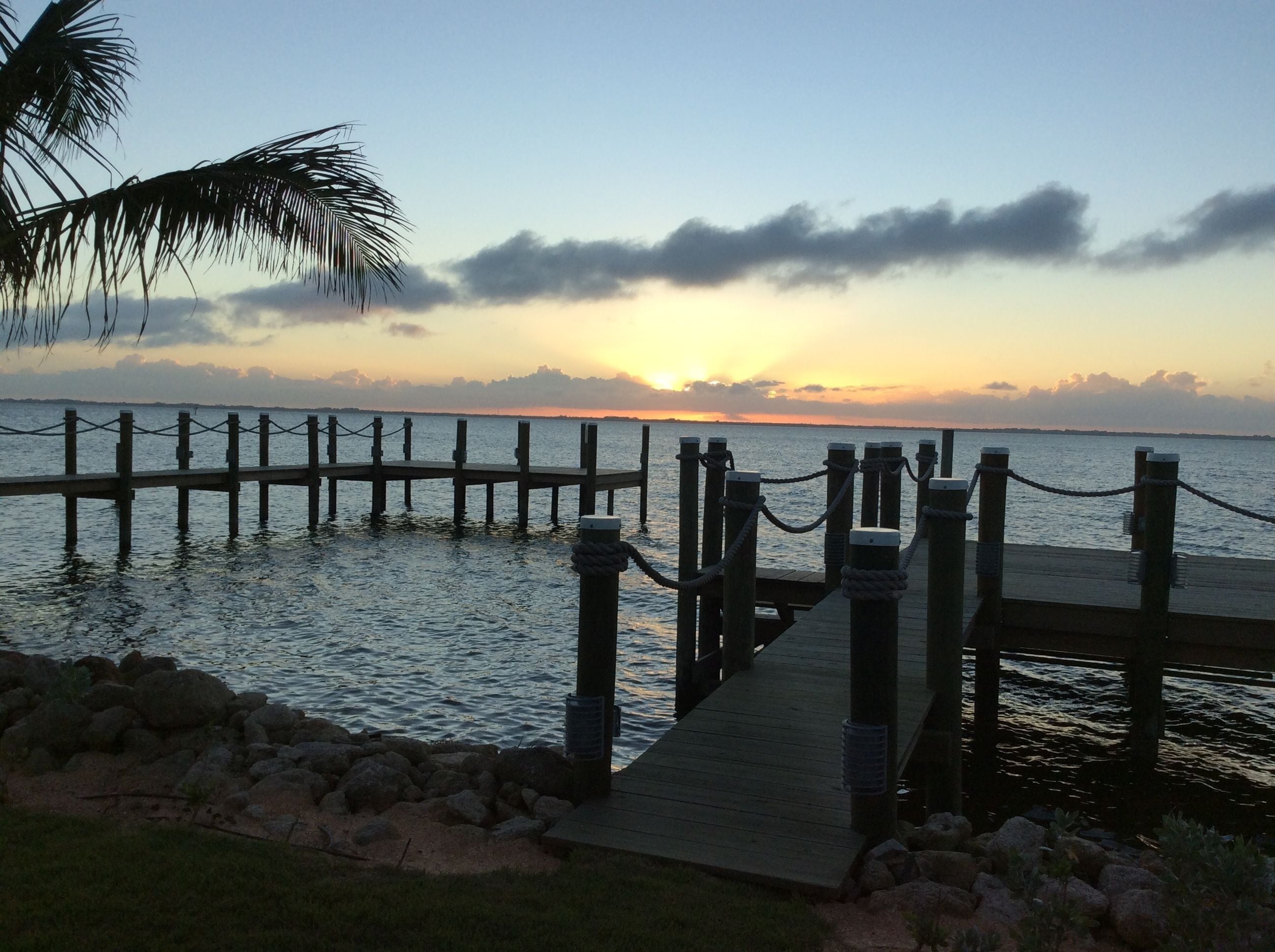 A wooden pier extending into calm water with a sunset in the background.