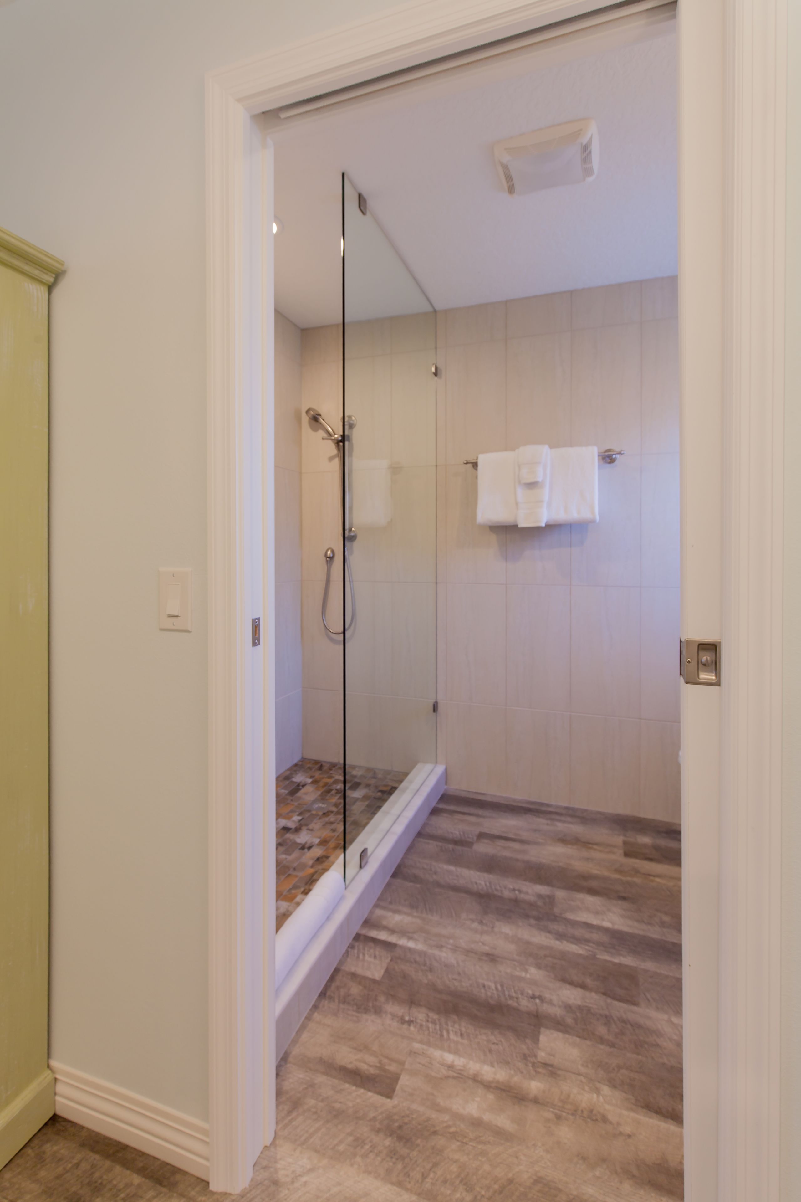 A walk-in shower with a glass door, a towel rack, and a wooden floor.