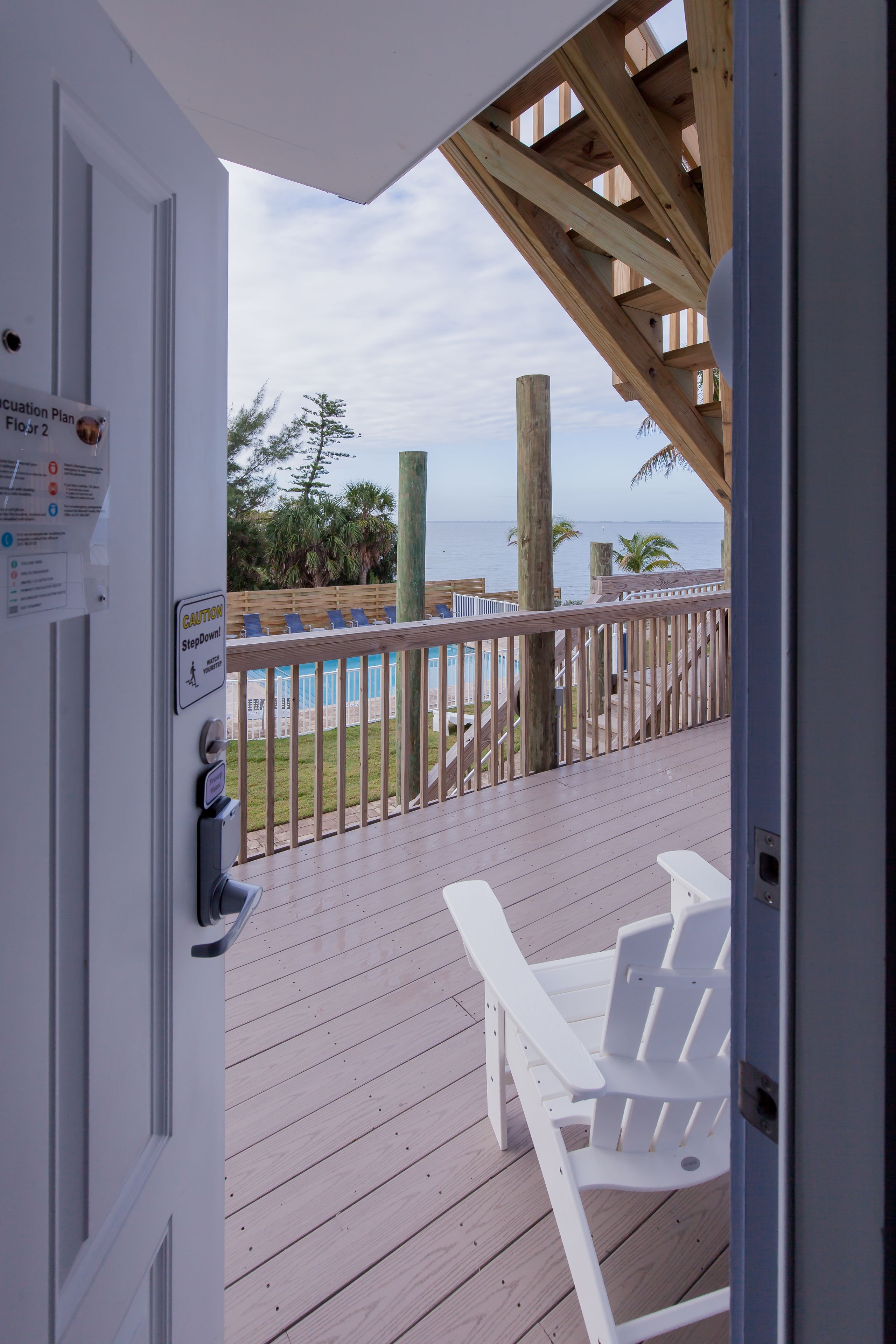 A wooden deck with white chairs, a wooden railing, and a view of the ocean.