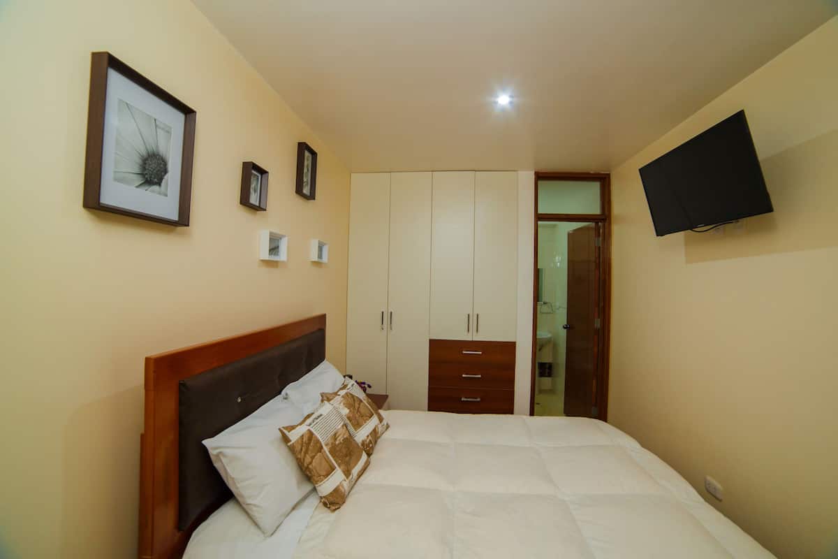 A bedroom with a bed, a wardrobe, a television mounted on the wall, and a framed picture on the wall.