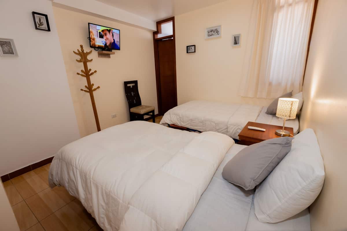 A hotel room with two beds, a TV mounted on the wall, a coat rack, and a window with curtains.