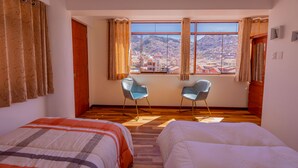 A hotel room with two beds, a window with a city view, and two chairs. - Cozy Room Cusco (Cusco)