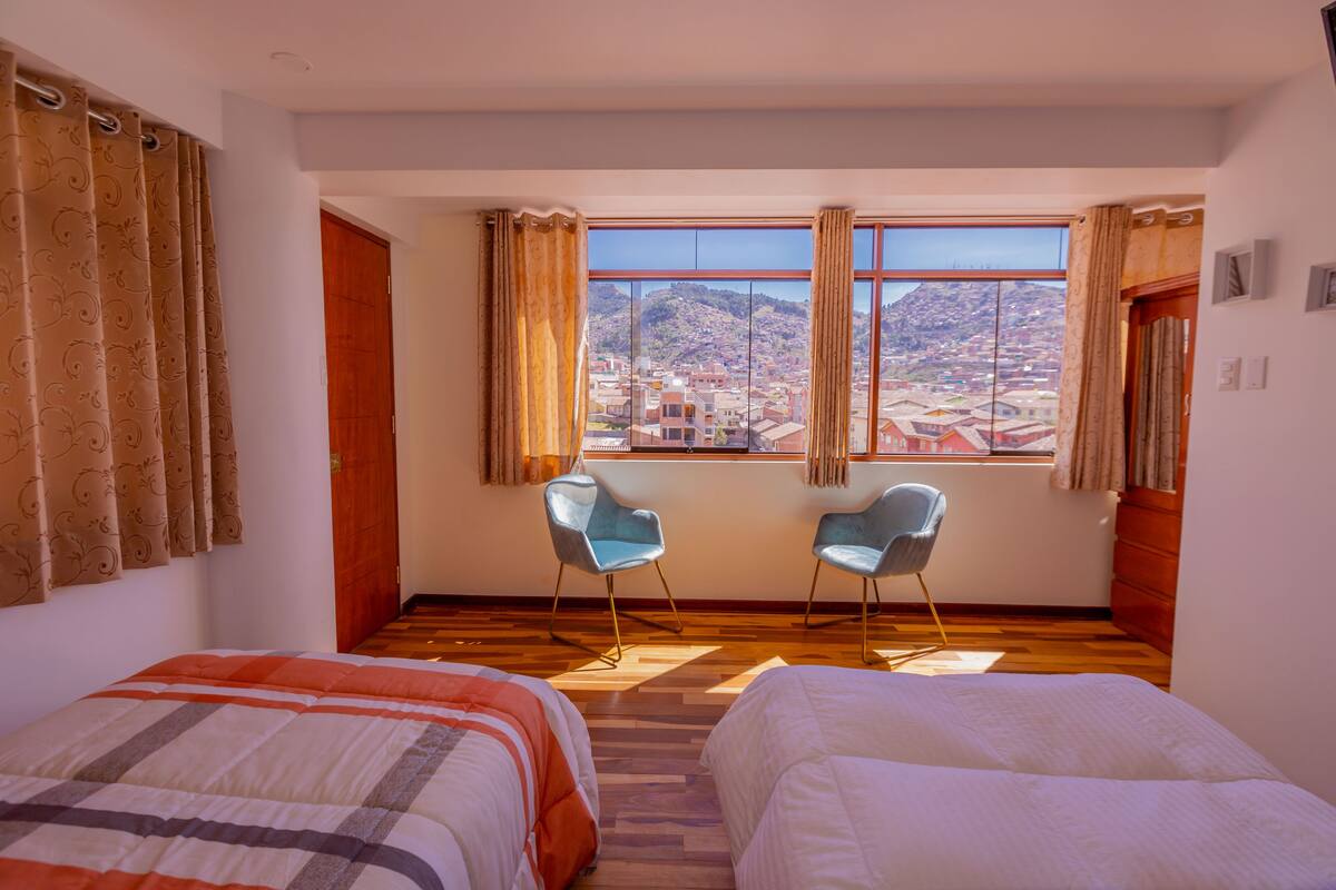 A hotel room with two beds, a window with a city view, and two chairs.