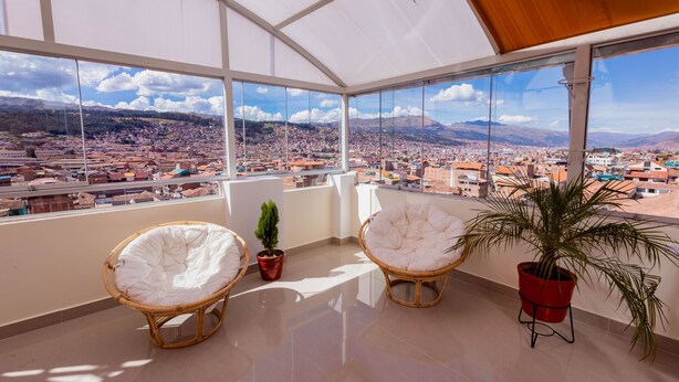 A balcony with two wicker chairs, a potted plant, and a city view. - Cozy Room Cusco (Cusco)