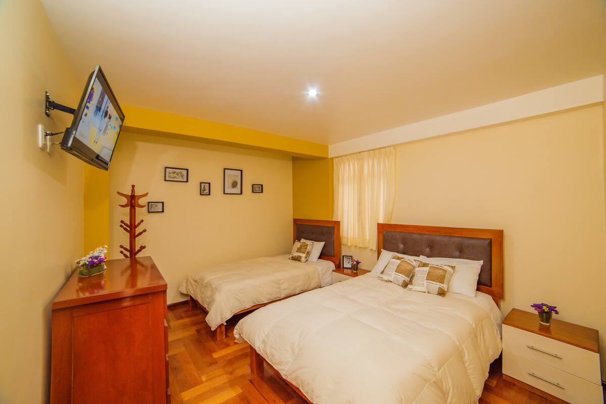 A hotel room with two beds, a desk, a flat-screen TV mounted on the wall, and a wooden dresser.