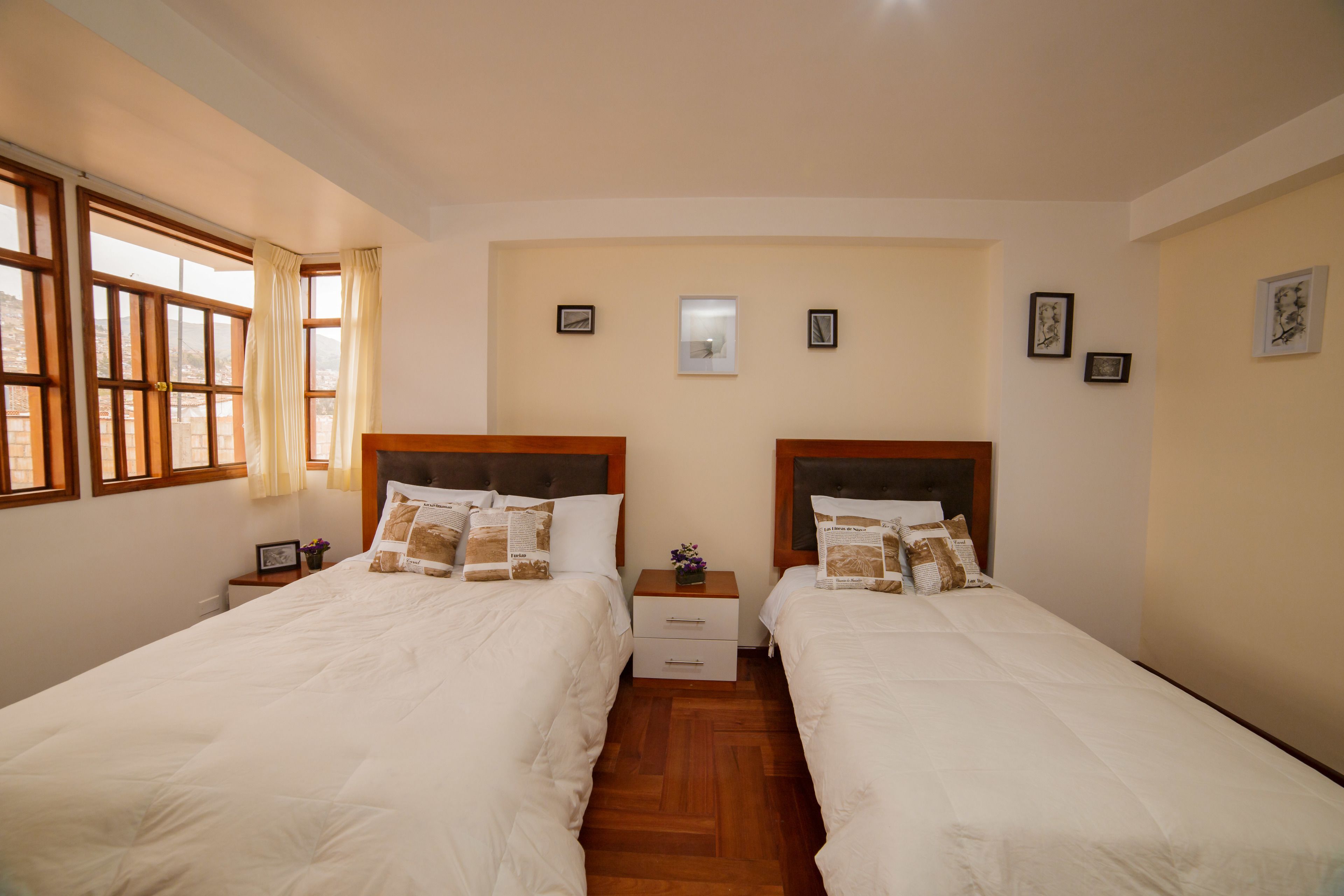 A double room with two beds, wooden headboards, a small bedside table with a lamp, and a window with curtains.