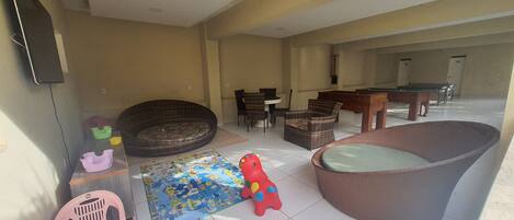 A living room with a pool table, wicker furniture, and a children's play area.
