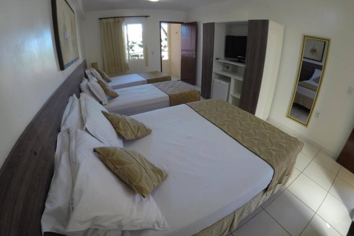 A hotel room with two beds, a TV, a mirror, and a window with curtains.