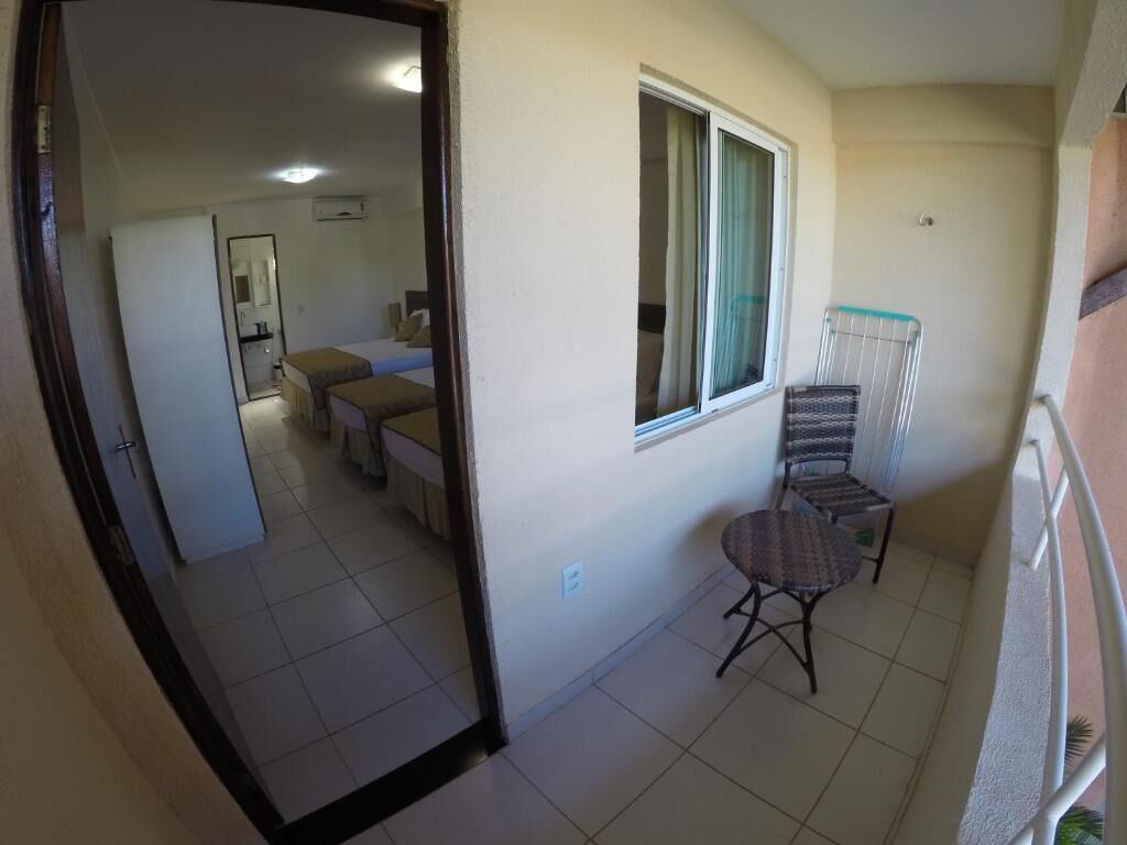 Un piccolo balcone con una sedia e un tavolo, una finestra con tende e un pavimento piastrellato.