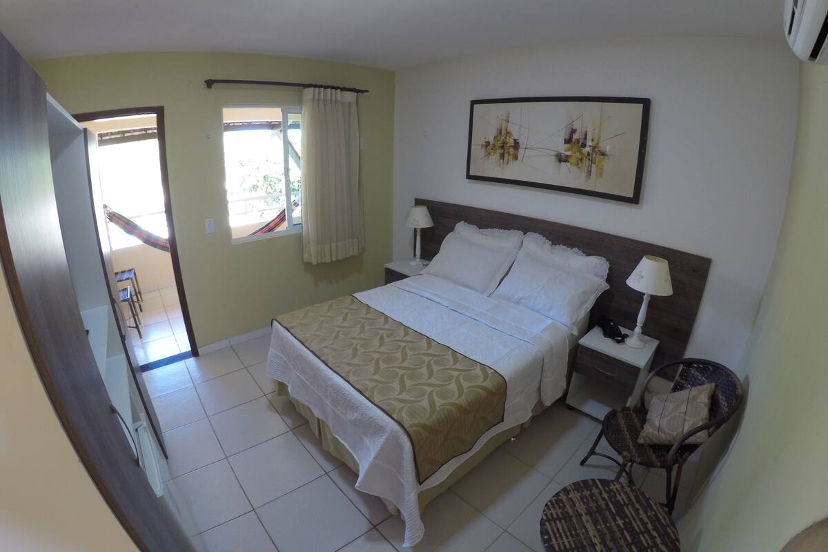 A hotel room with a bed, bedside tables, a chair, a window with curtains, and a painting on the wall.