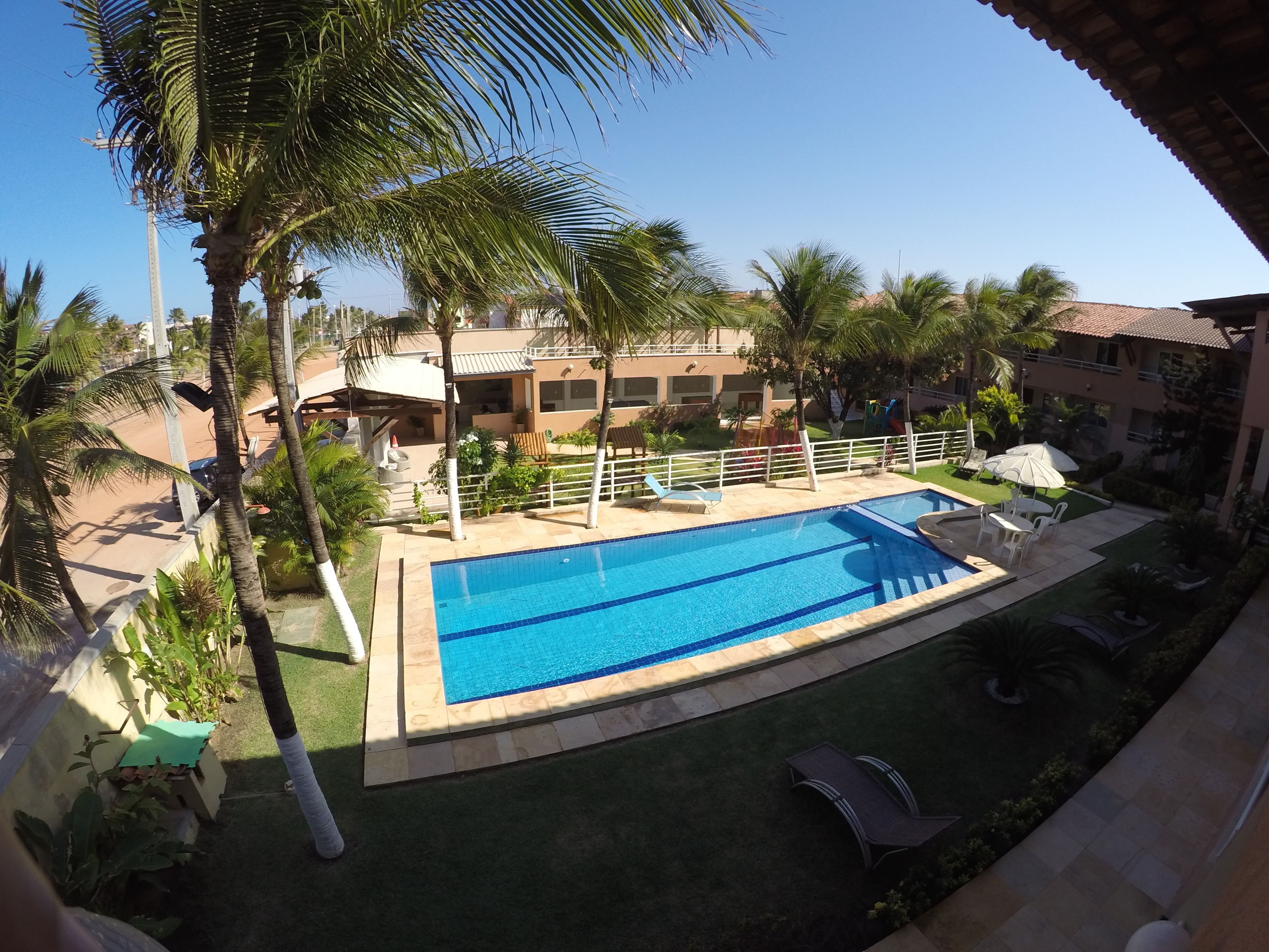 A swimming pool with lounge chairs and palm trees, surrounded by buildings.