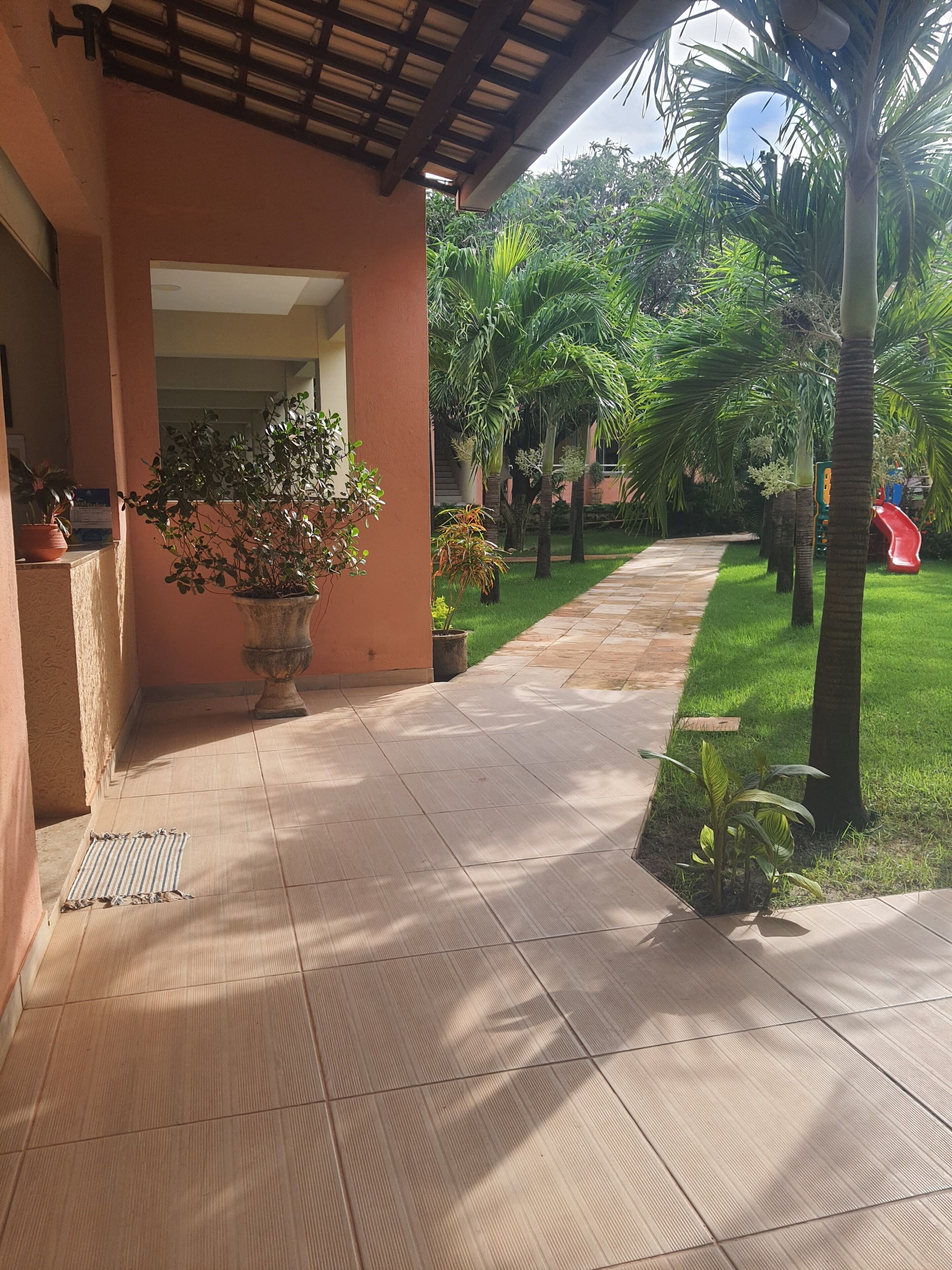 A covered outdoor area with a tiled walkway, potted plants, and a playground.