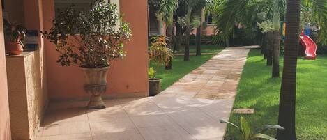 A covered outdoor area with a tiled walkway, potted plants, and a playground.