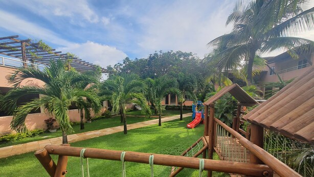 A playground area with a slide, surrounded by palm trees and a wooden fence. - Pousada Porto das Dunas (Aquiraz)
