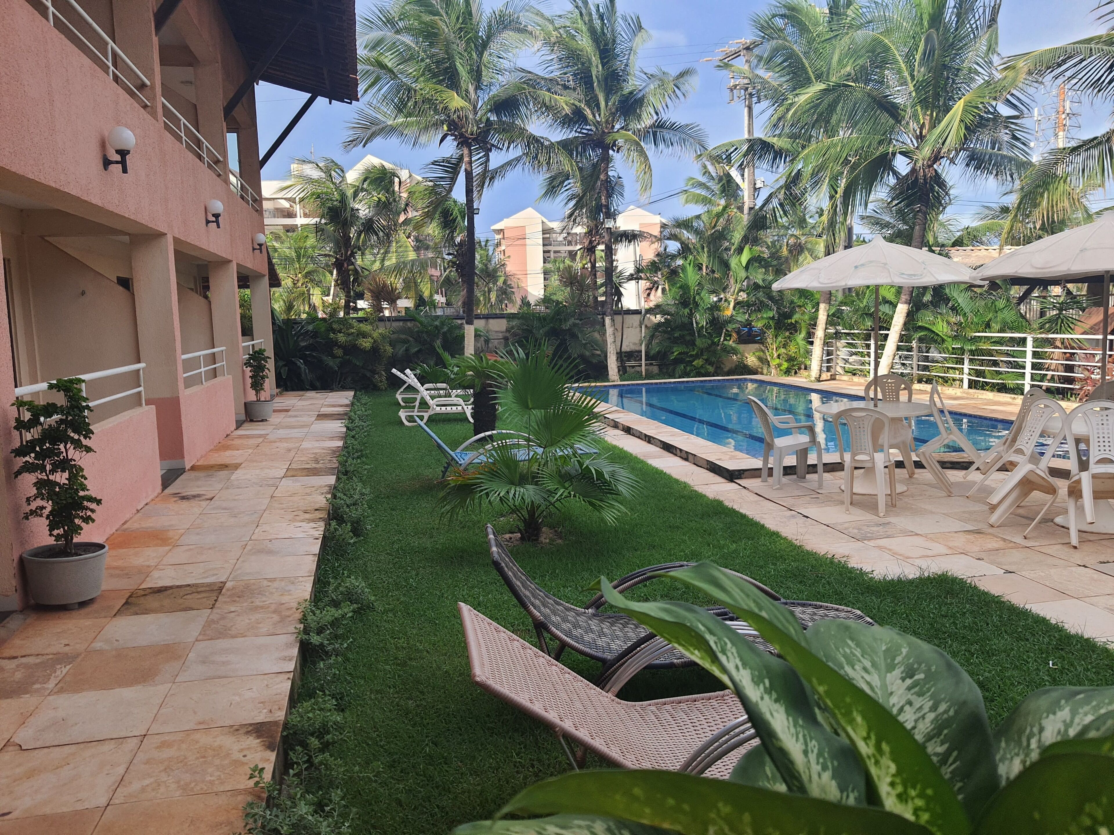 A pool area with lounge chairs, a small garden, and a building with a pink facade.
