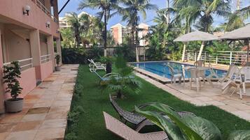 A pool area with lounge chairs, a small garden, and a building with a pink facade.