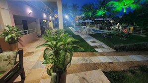 An outdoor area with a pool, palm trees, and a seating area with chairs and umbrellas. - Pousada Porto das Dunas (Aquiraz)
