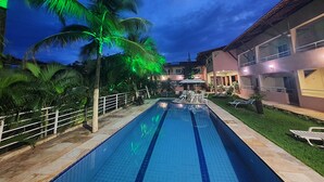 A swimming pool with a tiled edge, surrounded by palm trees and a building with balconies. - Pousada Porto das Dunas (Aquiraz)