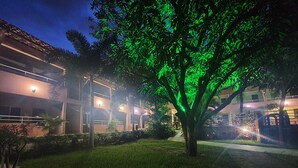 A building with a two-story structure, a well-maintained lawn, and a tree with illuminated green foliage. - Pousada Porto das Dunas (Aquiraz)
