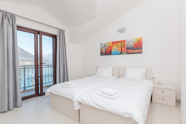 A bedroom with a large bed, a nightstand, and a view of a mountain through a sliding glass door. - Apartments Miramar (Kotor)
