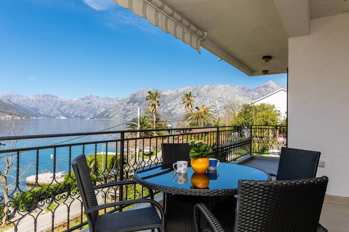Un balcón con mesa y sillas, con vistas a un lago y montañas.
