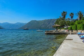 Escena costera con muelle, barcos y montañas al fondo.