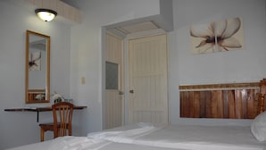 Een slaapkamer met een bed, een houten hoofdbord, een bureau met stoel, een spiegel en een deur.