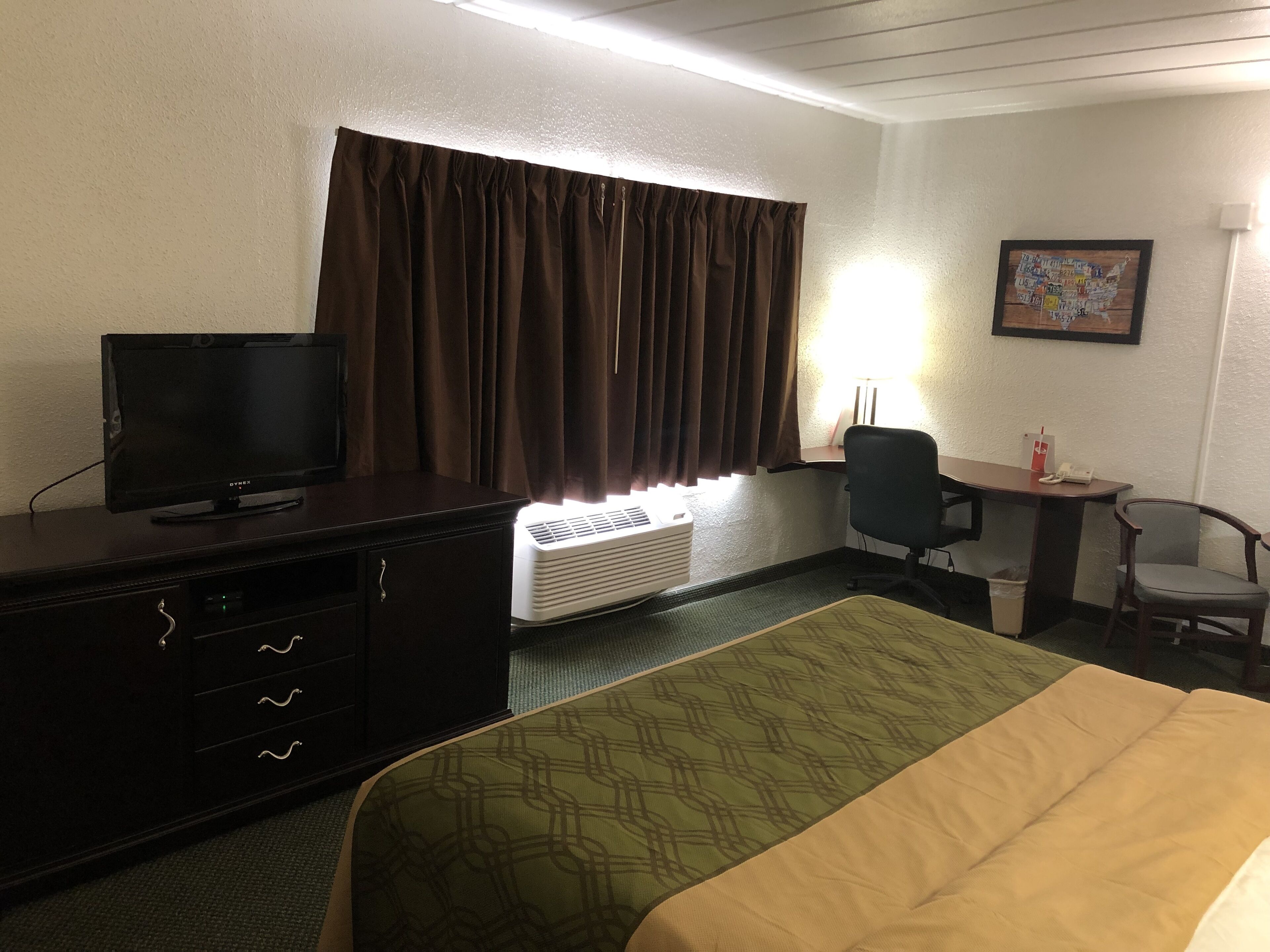 Una habitació d'hotel amb un llit, escriptori amb cadira, televisió i aire condicionat.