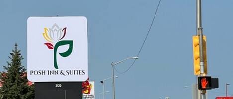 Señal de POSH INN & SUITES, con logotipo, situada en una intersección con semáforos y una calle visible.