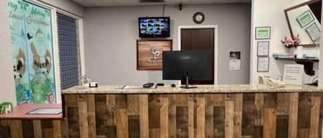 A reception desk with a wooden panel design, a television mounted on the wall, and a clock above the door.