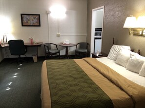 A hotel room with a bed, a desk, two chairs, a small table, and a wall-mounted lamp.