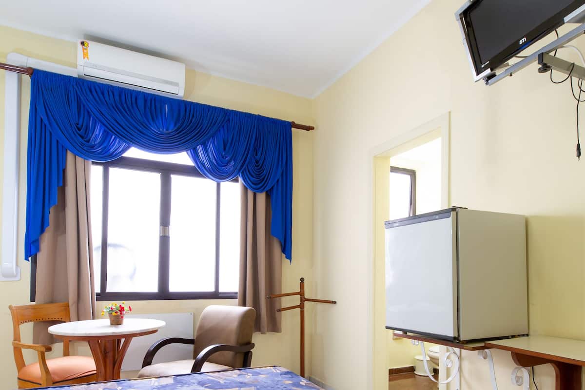 A hotel room with a bed, a desk, a chair, a television, and an air conditioning unit.