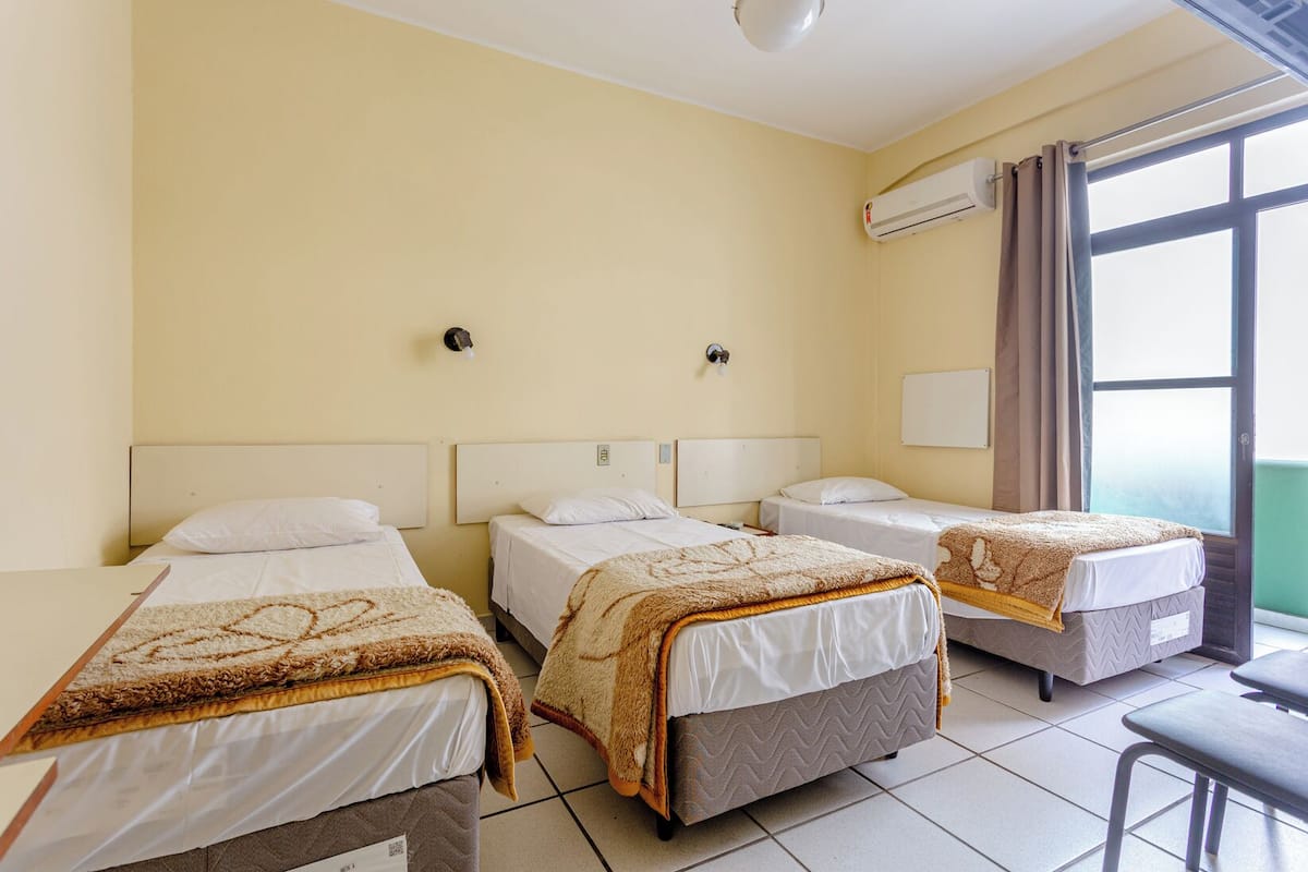 A hotel room with three single beds, a small table, and a window with curtains.