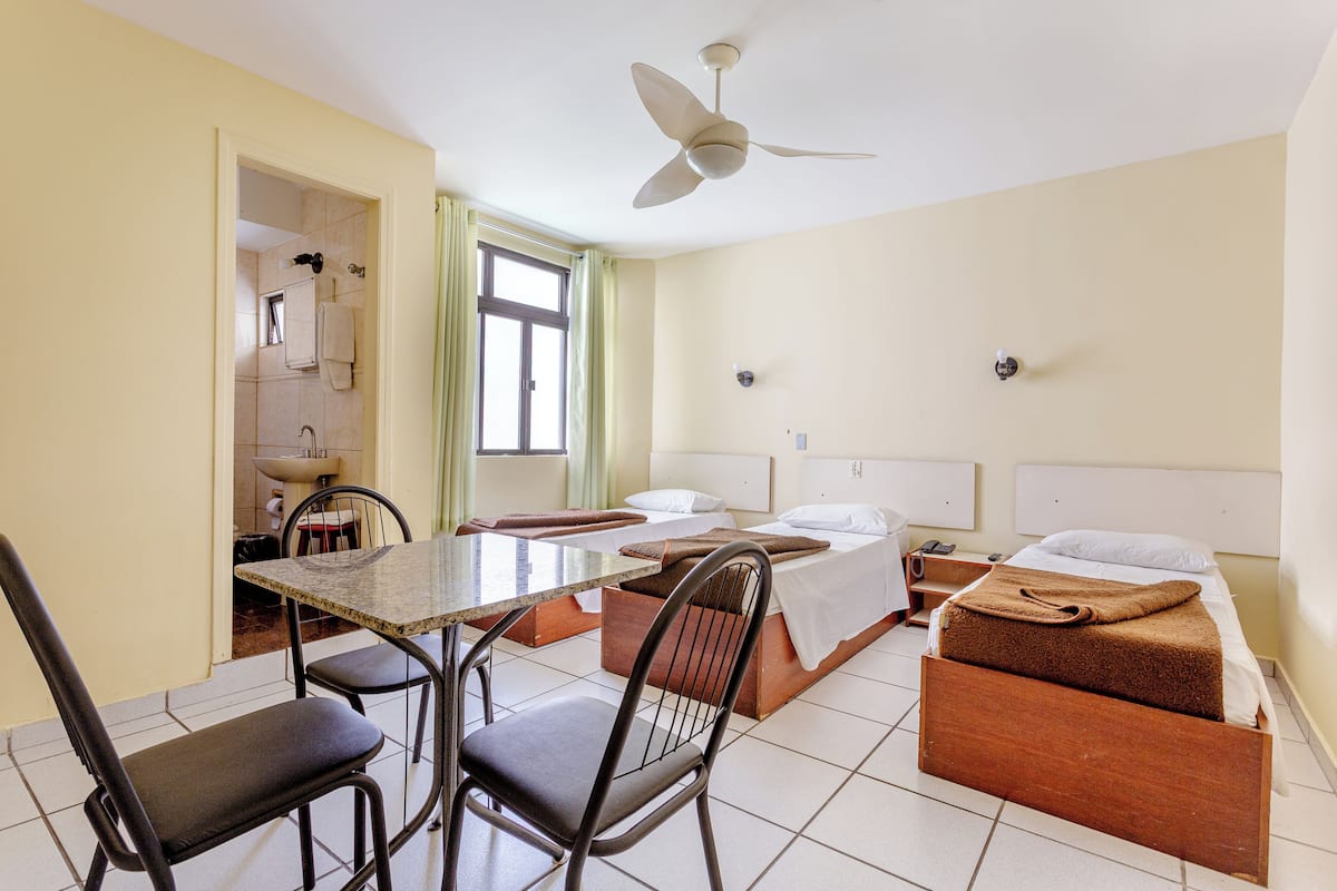 A hotel room with a bed, a table with chairs, a ceiling fan, and a view of the bathroom.